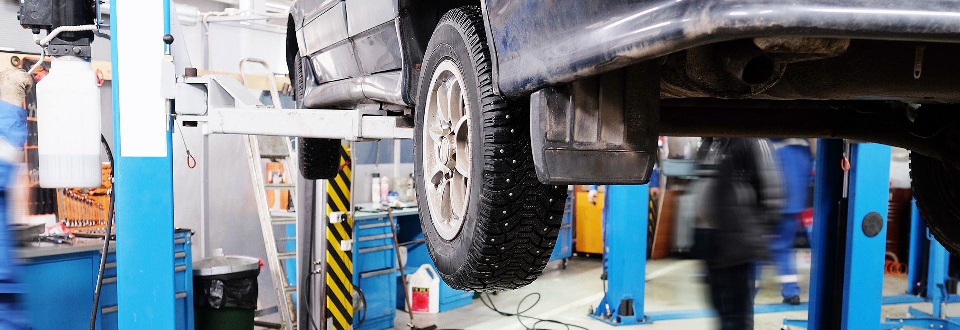 Werkstatt mit einem Auto auf einer Hebebühne und mehreren Personen, die daran arbeiten