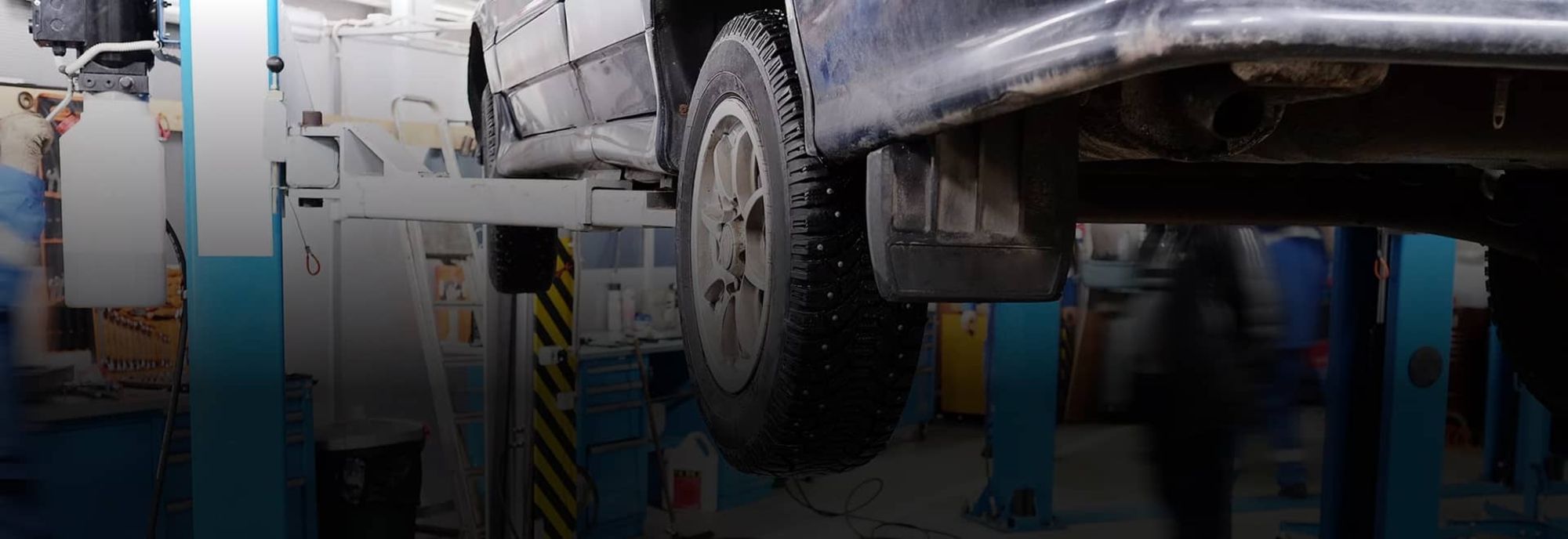Unter einem auf einer Hebebühne angehobenen Auto ist ein Mechaniker in einer Werkstatt zu sehen 1 (1)